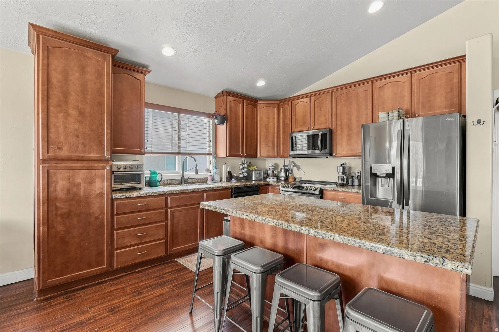 Kitchen featuring extensive wood cabinetry, granite countertops, wood-finish flooring, a stainless steel refrigerator, and recessed lighting