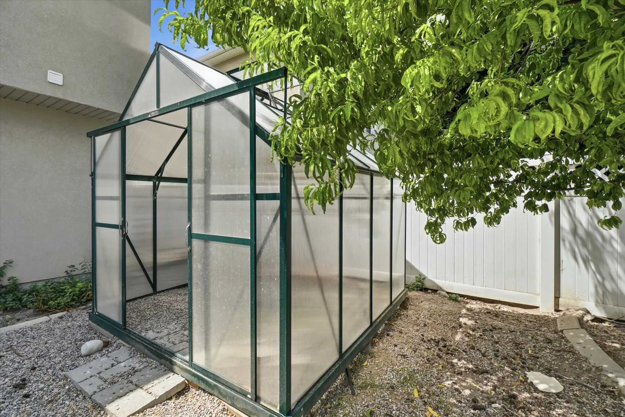 Gabled greenhouse with a dark frame and clear paneling, featuring a gravel floor and a stone paver path