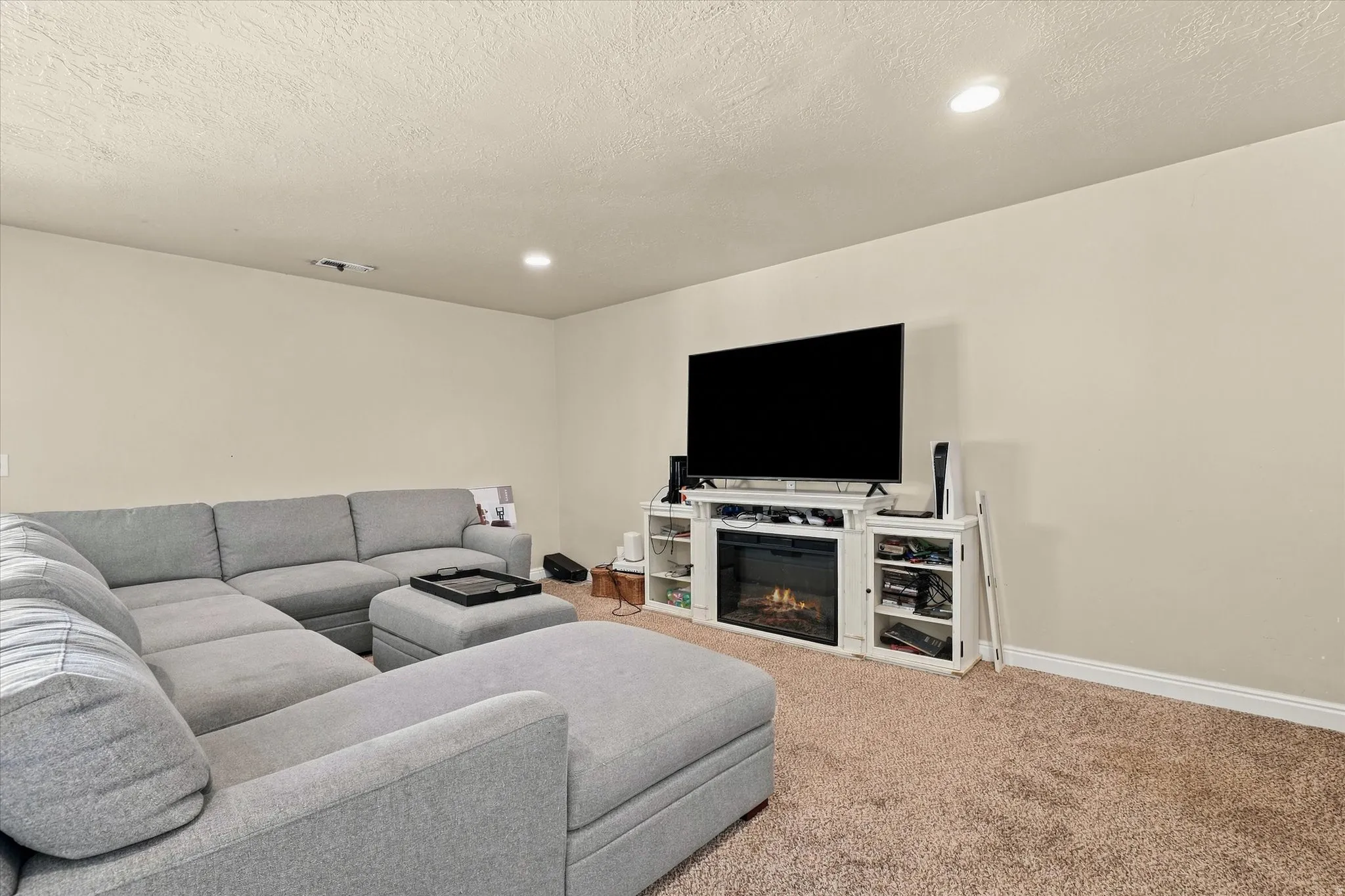 Recessed lighting illuminates a carpeted room featuring an entertainment center with an electric fireplace