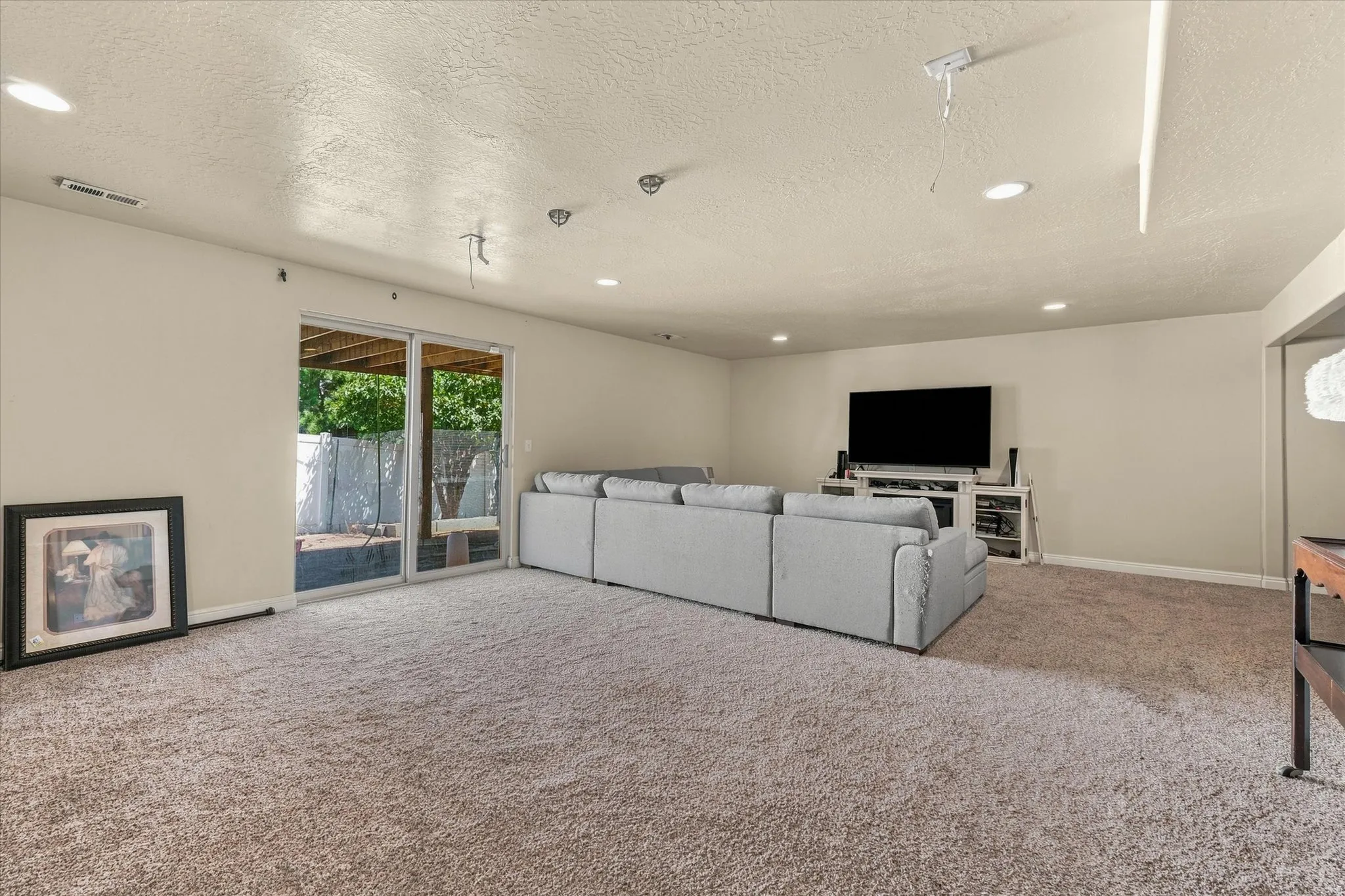 Spacious finished lower-level room featuring neutral-toned carpeting, recessed lighting, and a large sliding glass door