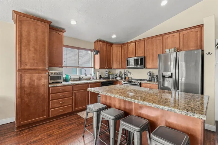 Kitchen featuring extensive wood cabinetry, granite countertops, wood-finish flooring, a stainless steel refrigerator, and recessed lighting