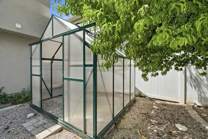 Gabled greenhouse with a dark frame and clear paneling, featuring a gravel floor and a stone paver path
