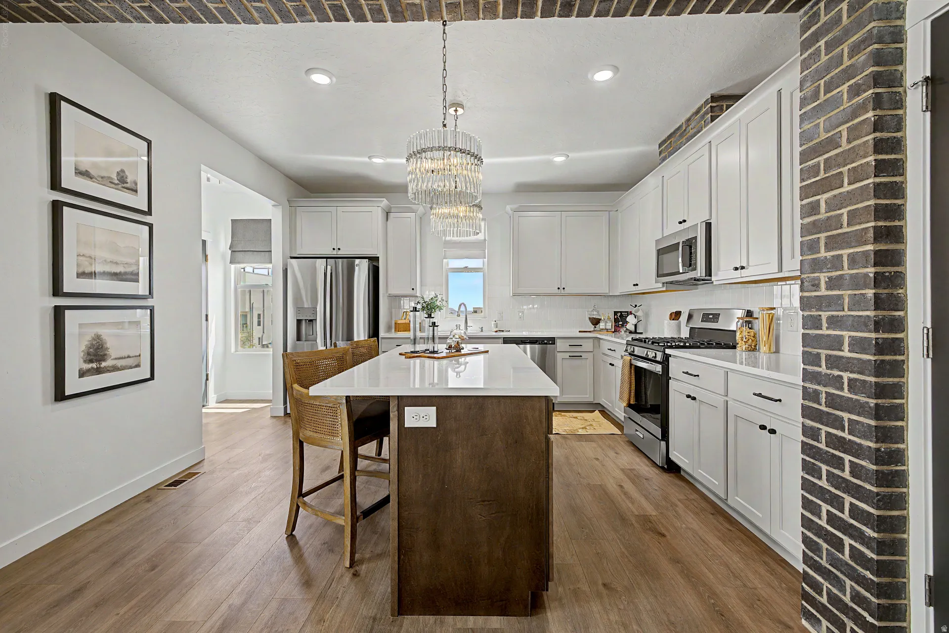 Bright kitchen featuring a central island with white countertop, white cabinetry with dark hardware, stainless steel appliances, and wood-finish flooring