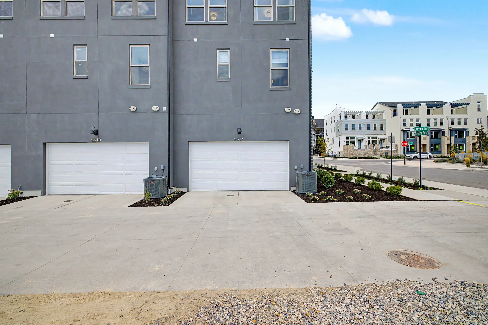 Modern multi-story facade featuring a gray stucco exterior, multiple white-framed windows, and two individual single-car garages with white sectional doors