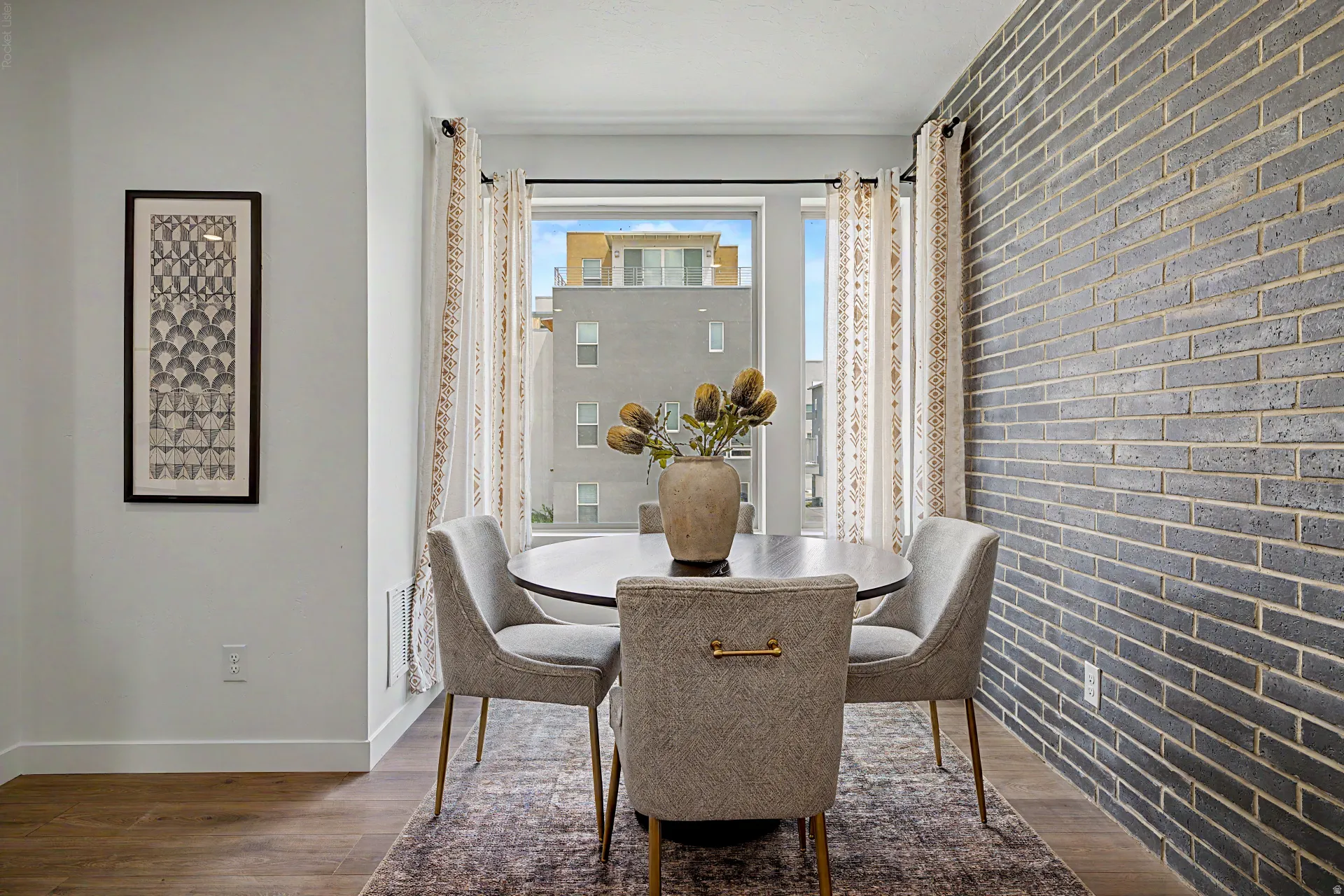 Dining area with an accent brick wall, large window, wood-finish flooring, and white trim