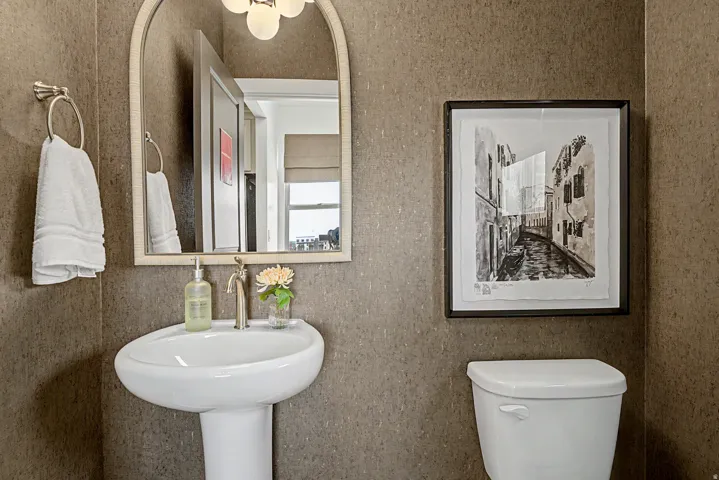 Pedestal sink with a brushed nickel faucet, arched vanity mirror, and wall-mounted light fixture