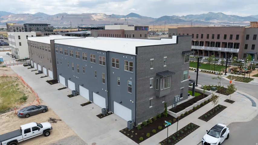Modern townhome exterior featuring multi-story design, a bay window with a dark metal awning, multiple windows with dark frames, a private garage door, and structured landscaping with young trees and shrubs