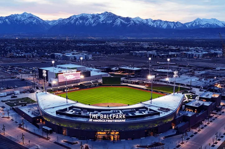 The Ballpark at America First Square featuring a vibrant green field, stadium lighting, and surrounding urban development with a prominent mountain range backdrop