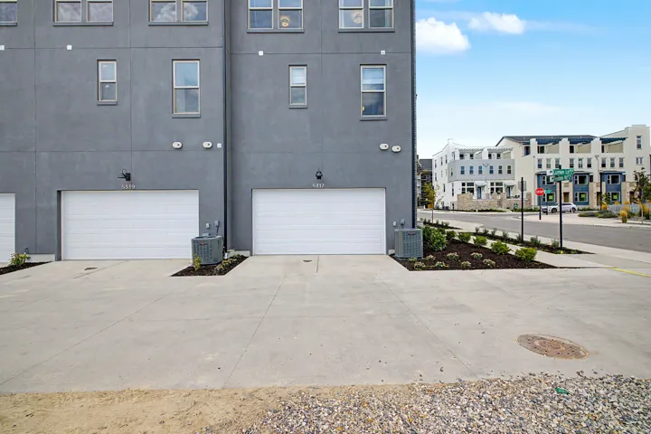 Modern multi-story facade featuring a gray stucco exterior, multiple white-framed windows, and two individual single-car garages with white sectional doors
