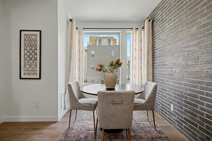 Dining area with an accent brick wall, large window, wood-finish flooring, and white trim