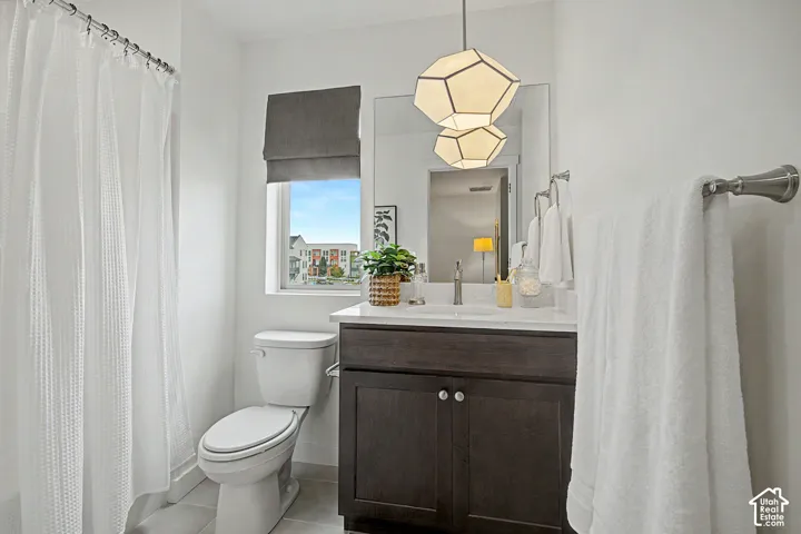 Bathroom featuring a modern geometric pendant light, a dark wood-finish vanity with a white countertop and undermount sink, a large wall mirror, and a window with a Roman shade