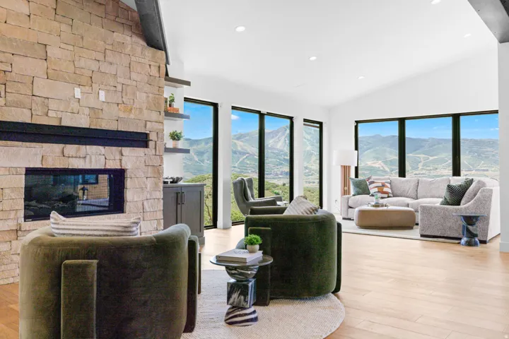 Spacious living area featuring a stone-clad fireplace, vaulted ceiling, and wood-finish flooring