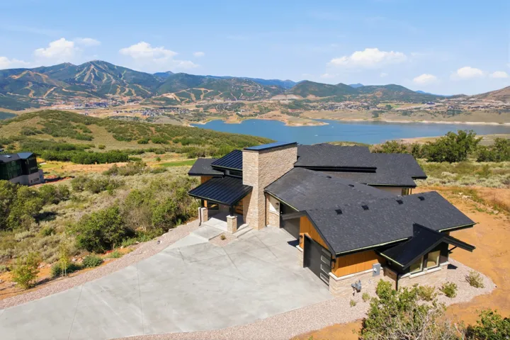 Contemporary residence featuring a prominent stone chimney, dark shingled roofing, and a concrete driveway