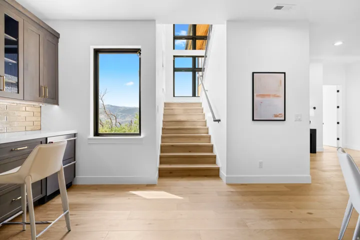 Hardwood flooring extending through the space, featuring a built-in wet bar with dark cabinetry, a subway tile backsplash, and a white countertop
