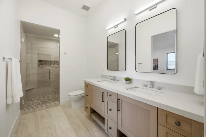 Bathroom featuring a dual vanity with light wood-finish cabinetry, white countertop, and polished chrome fixtures