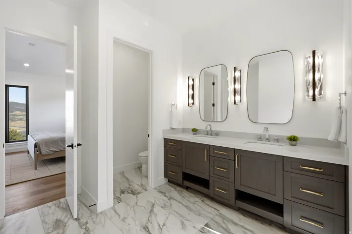 Dual vanity featuring dark wood cabinetry with gold hardware, two rectangular mirrors, and stylish wall sconces
