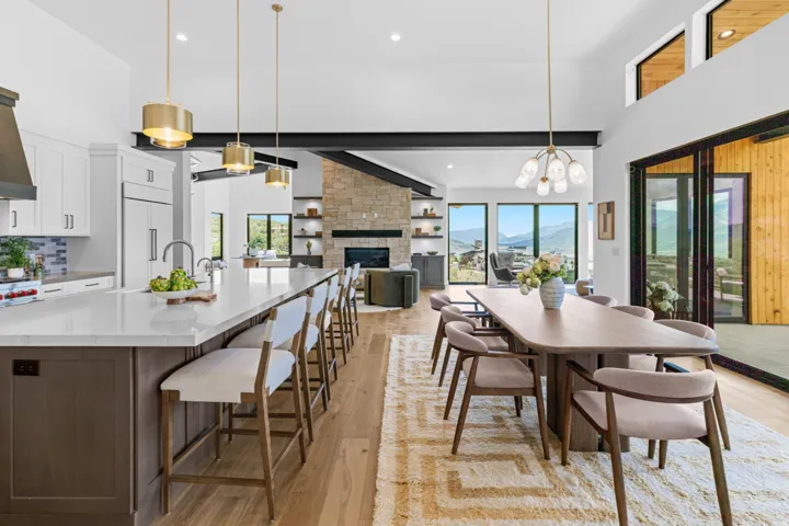 Open-concept living area featuring a spacious kitchen island with seating, pendant lighting, hardwood flooring, a stone fireplace, and large sliding glass doors