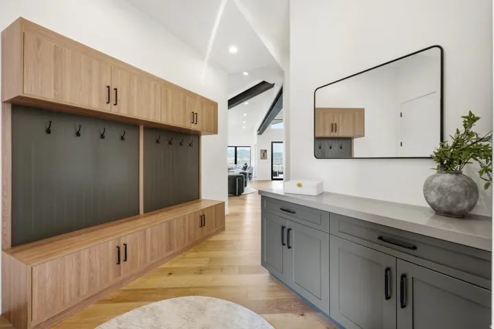Entryway featuring wood-finish flooring, built-in cabinetry with black hardware, a dedicated coat rack area, and a built-in console table with a stone-finish countertop