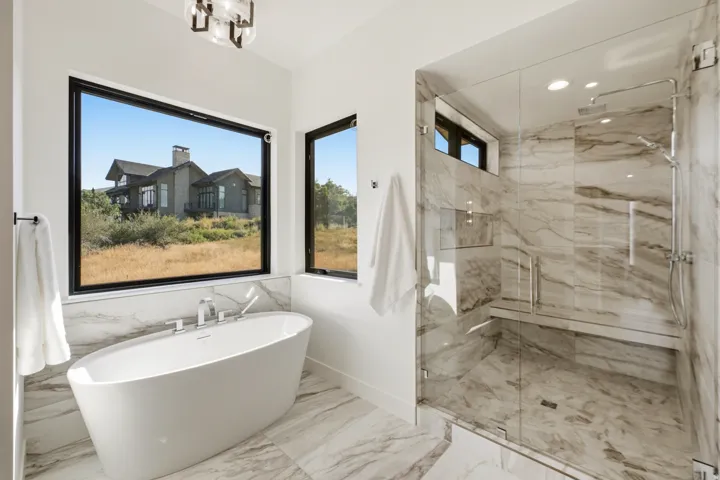 Bathroom featuring a freestanding oval soaking tub with chrome fixtures, a spacious walk-in shower with a glass enclosure, built-in shower bench, and a dual-head shower system
