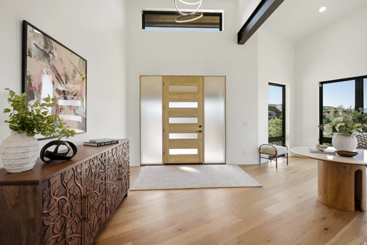 Spacious entry featuring a light wood-finish door with frosted glass sidelights, wood-finish flooring, and high ceilings with clerestory windows