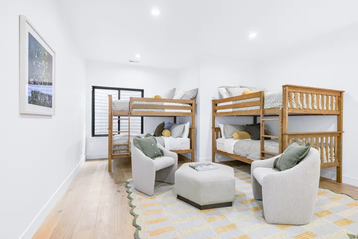 Bright, open bedroom featuring multiple wood-finish bunk beds with slatted headboards, light wood-tone framing, and coordinating bedding