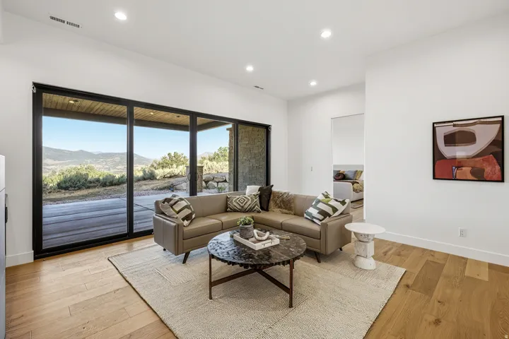 Spacious living area featuring expansive black-framed glass sliding doors, light wood-finish flooring, recessed lighting, and white walls