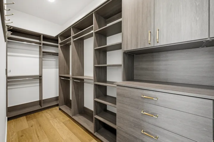 Custom walk-in closet featuring wood-finish organizational systems, integrated shelving, multiple hanging rods, built-in drawers, and overhead cabinetry with gold-tone hardware
