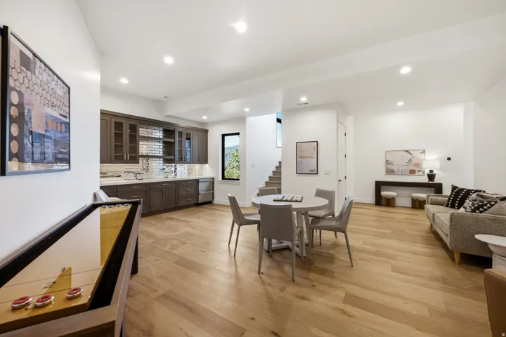 Spacious room featuring wood-finish flooring, a built-in wet bar with dark cabinetry and a tiled backsplash, recessed lighting, and a window providing exterior views