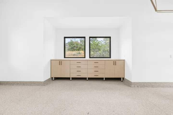 Built-in wood-finish cabinetry featuring multiple drawers and door storage, set beneath two black-framed windows