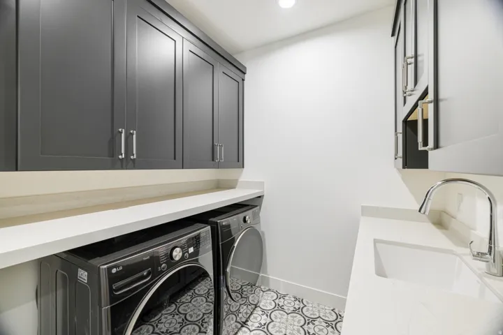 Laundry room featuring dark gray cabinetry with brushed nickel hardware, white countertops, a built-in utility sink with a chrome faucet, and decorative floor tiling