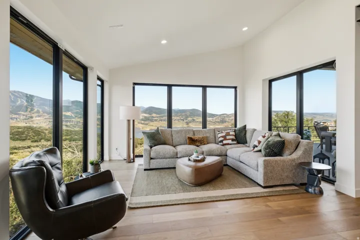 Living space featuring expansive floor-to-ceiling windows, natural wood-finish flooring, a clean white color palette, recessed lighting, and a high vaulted ceiling