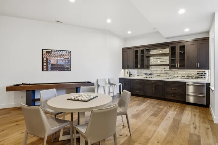 Spacious entertainment area featuring wood-finish flooring, a full wet bar with dark cabinetry, integrated stainless steel appliances, and a mirrored subway tile backsplash