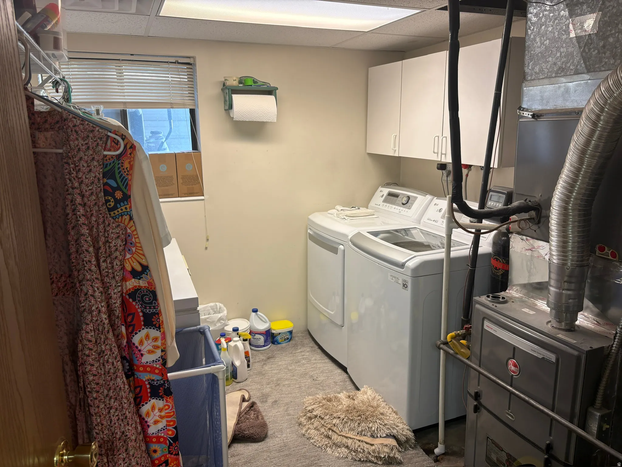 Utility room featuring a window with blinds, white upper cabinetry, and carpet flooring