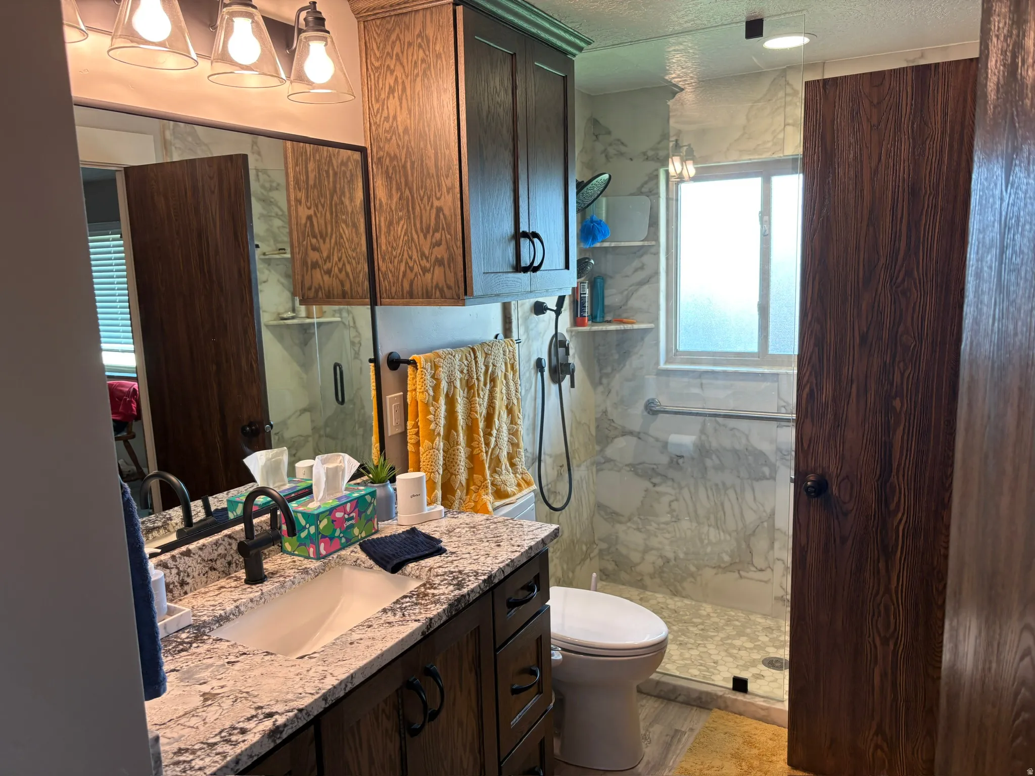 Bathroom featuring a granite-style countertop vanity with integrated sink, dark wood-finish cabinetry, and a walk-in shower