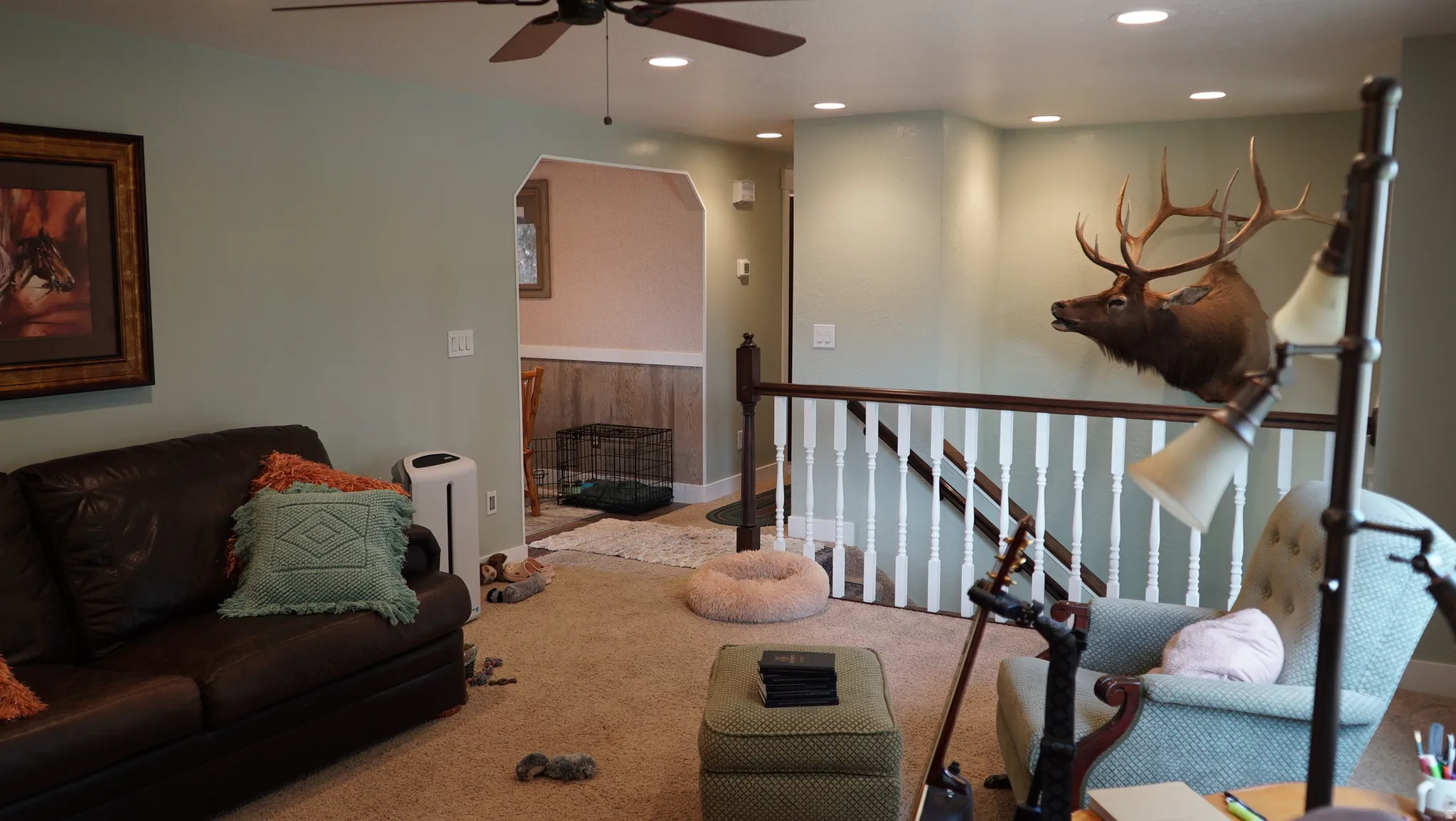 Living area featuring recessed lighting, a ceiling fan, carpet flooring, a wood-finish handrail, and a staircase with white spindles