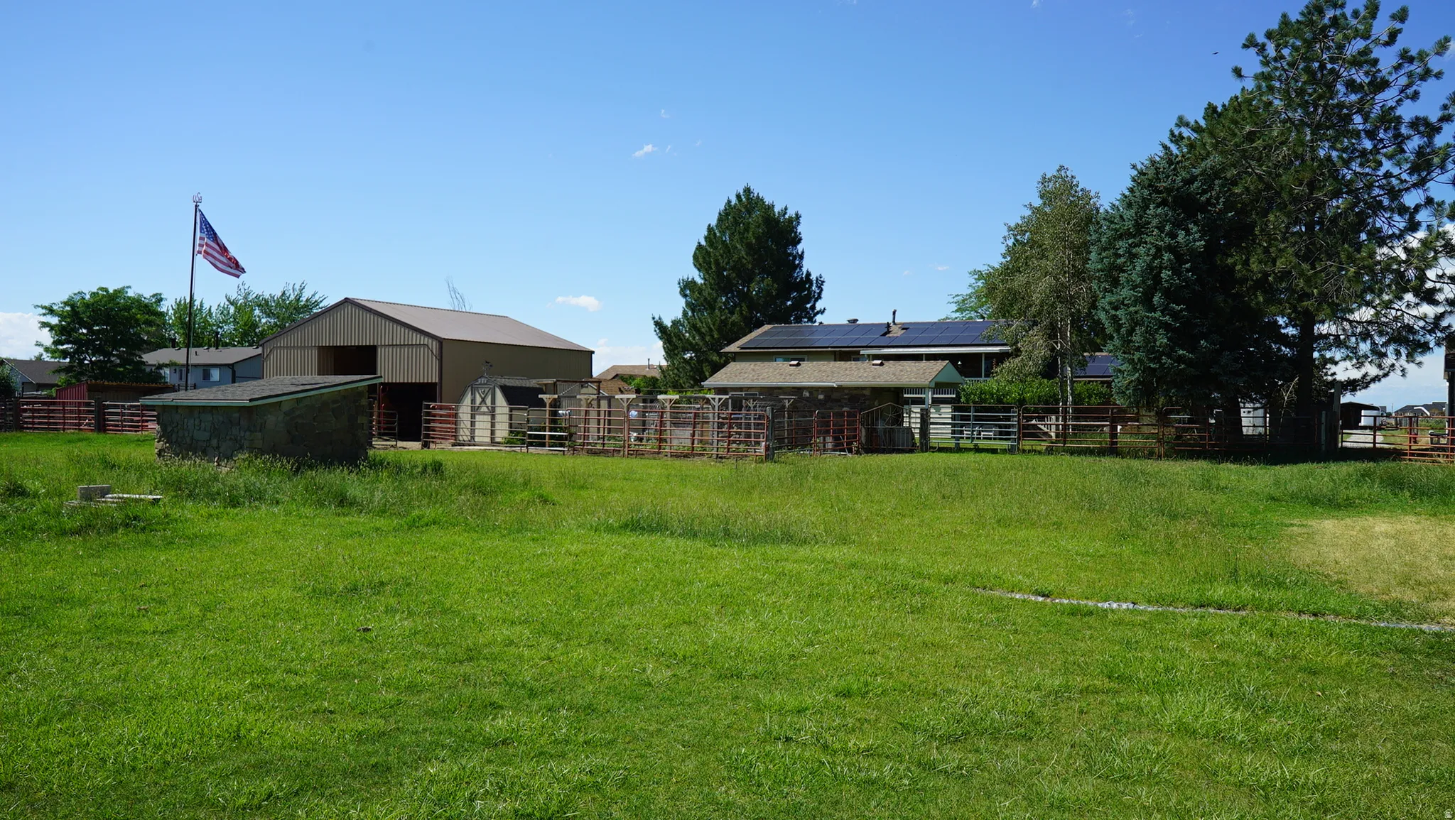 Expansive green lot featuring a large barn, multiple animal pens, a detached utility building, and mature trees