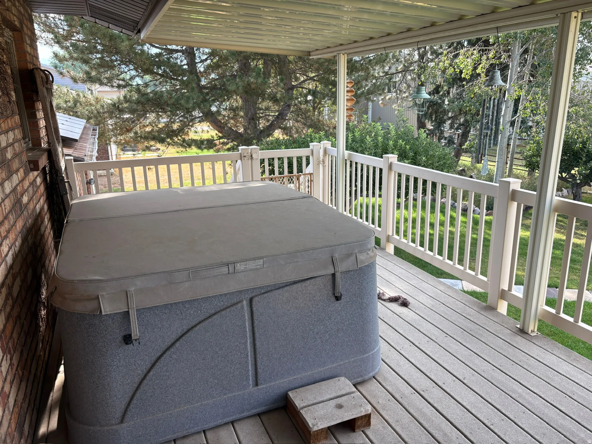 Covered outdoor patio deck featuring a built-in spa, wood-finish decking, white railings, and a brick exterior wall