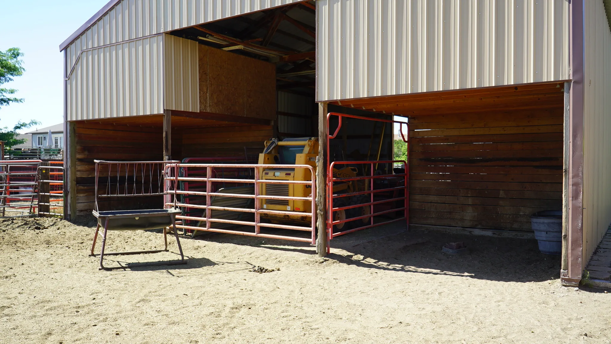 Metal-sided barn featuring multiple open bays, wood-paneled interiors, and red metal fencing
