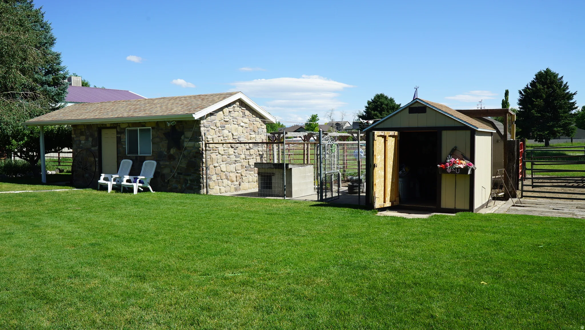 Manicured lawn with a stone-clad outbuilding featuring a covered patio, a built-in outdoor grill, and a separate storage shed