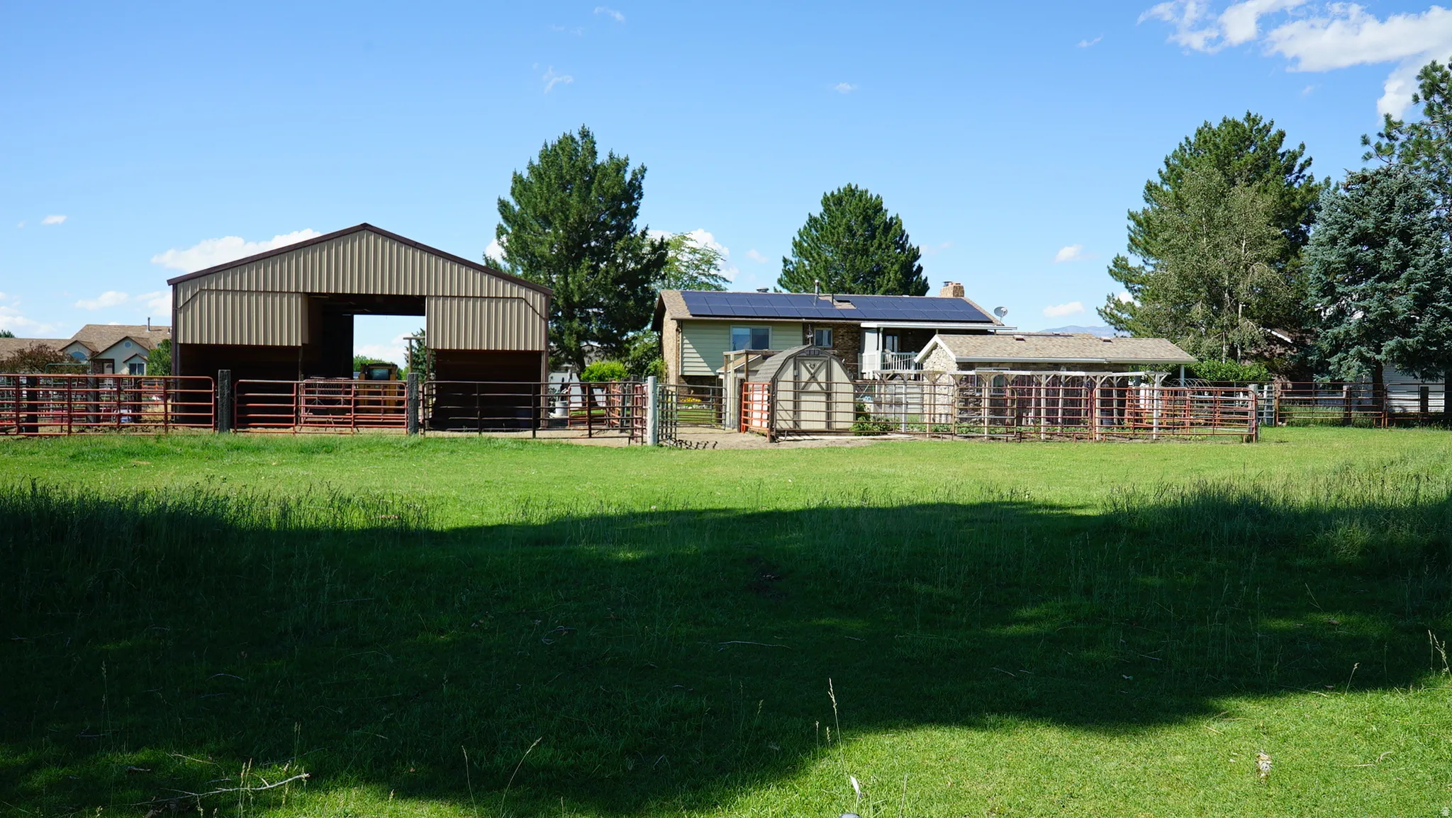 Expansive green space featuring a large barn structure with metal siding, multiple fenced areas, and mature trees