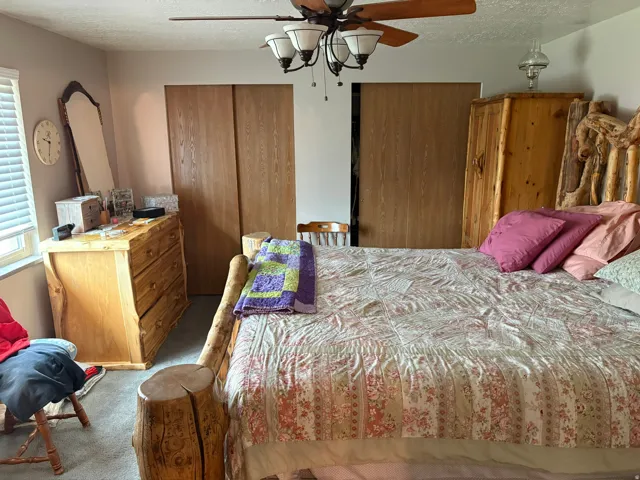 Carpeted room featuring a ceiling fan with integrated lighting, wood-finish sliding closet doors, and a window with blinds