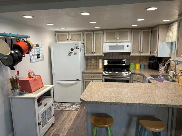 Open kitchen with recessed lighting, integrated stainless steel range and microwave, ample cabinetry, L-shaped countertop, and wood-finish flooring