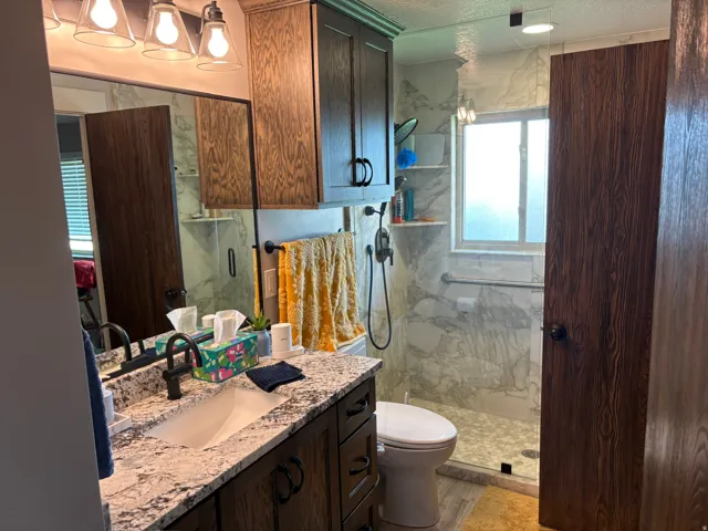 Bathroom featuring a granite-style countertop vanity with integrated sink, dark wood-finish cabinetry, and a walk-in shower