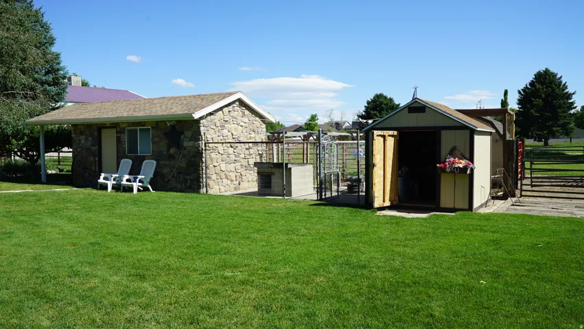 Manicured lawn with a stone-clad outbuilding featuring a covered patio, a built-in outdoor grill, and a separate storage shed