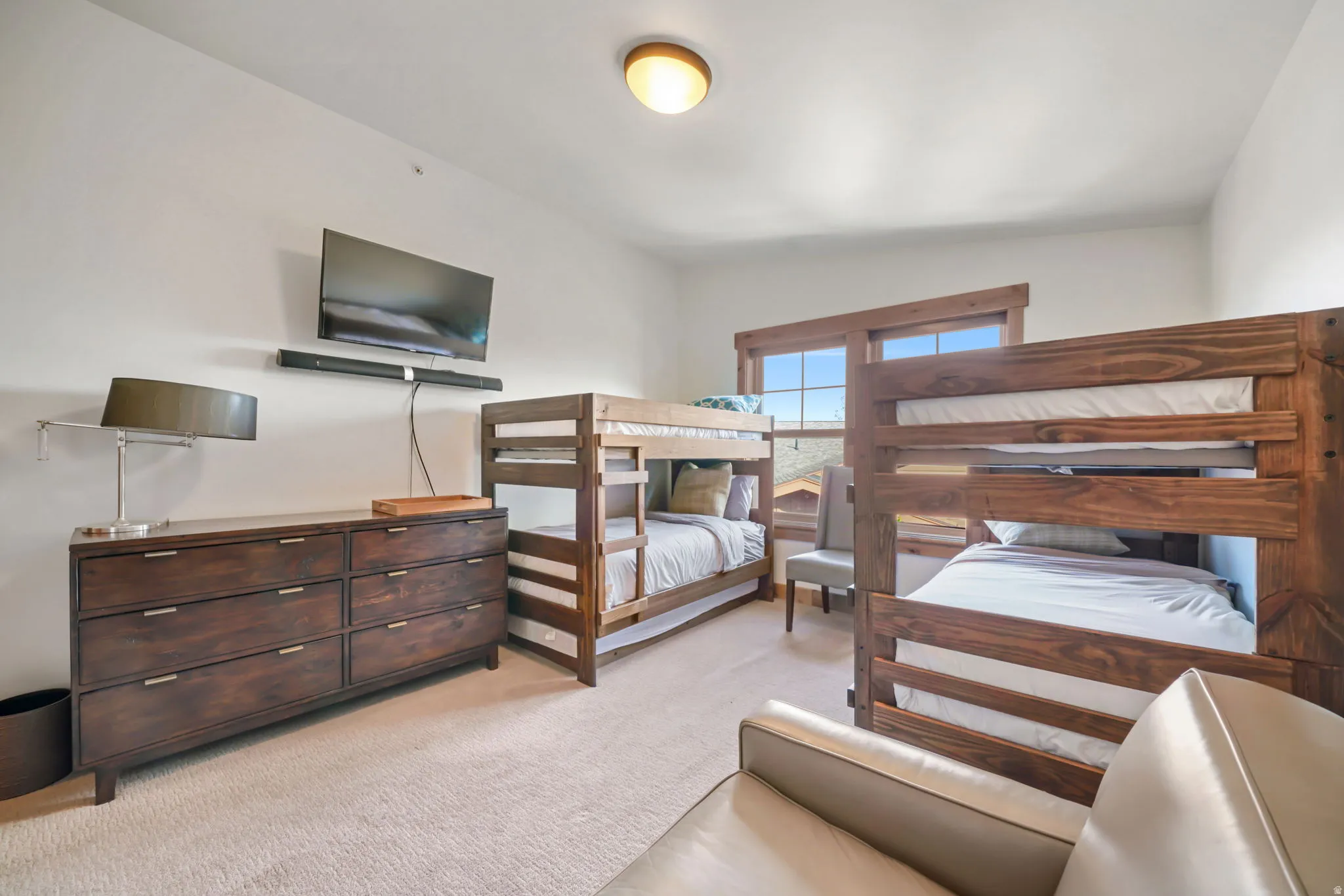Room featuring two wood-finish bunk beds, light-colored carpeting, and a built-in wall-mounted television