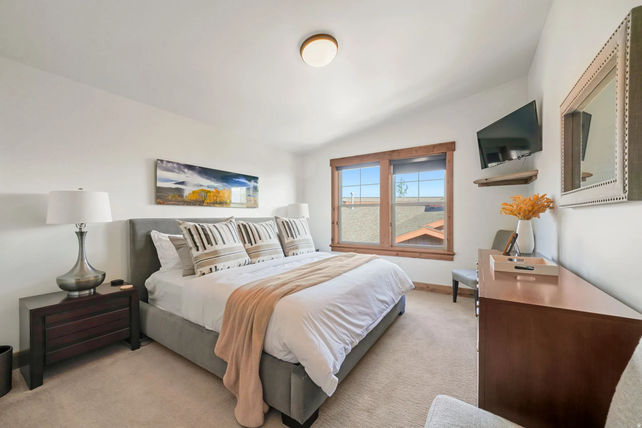 Bedroom featuring a wood-trimmed window, mounted television, wood-finish dresser, and carpeted flooring