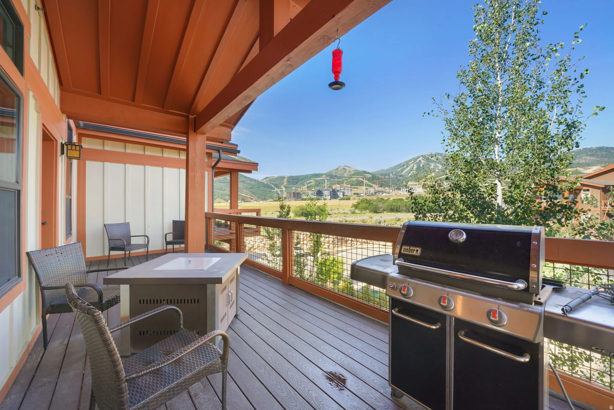 Expansive outdoor deck featuring wood-finish decking, a built-in fire table, and a protective overhang with exposed wood beams