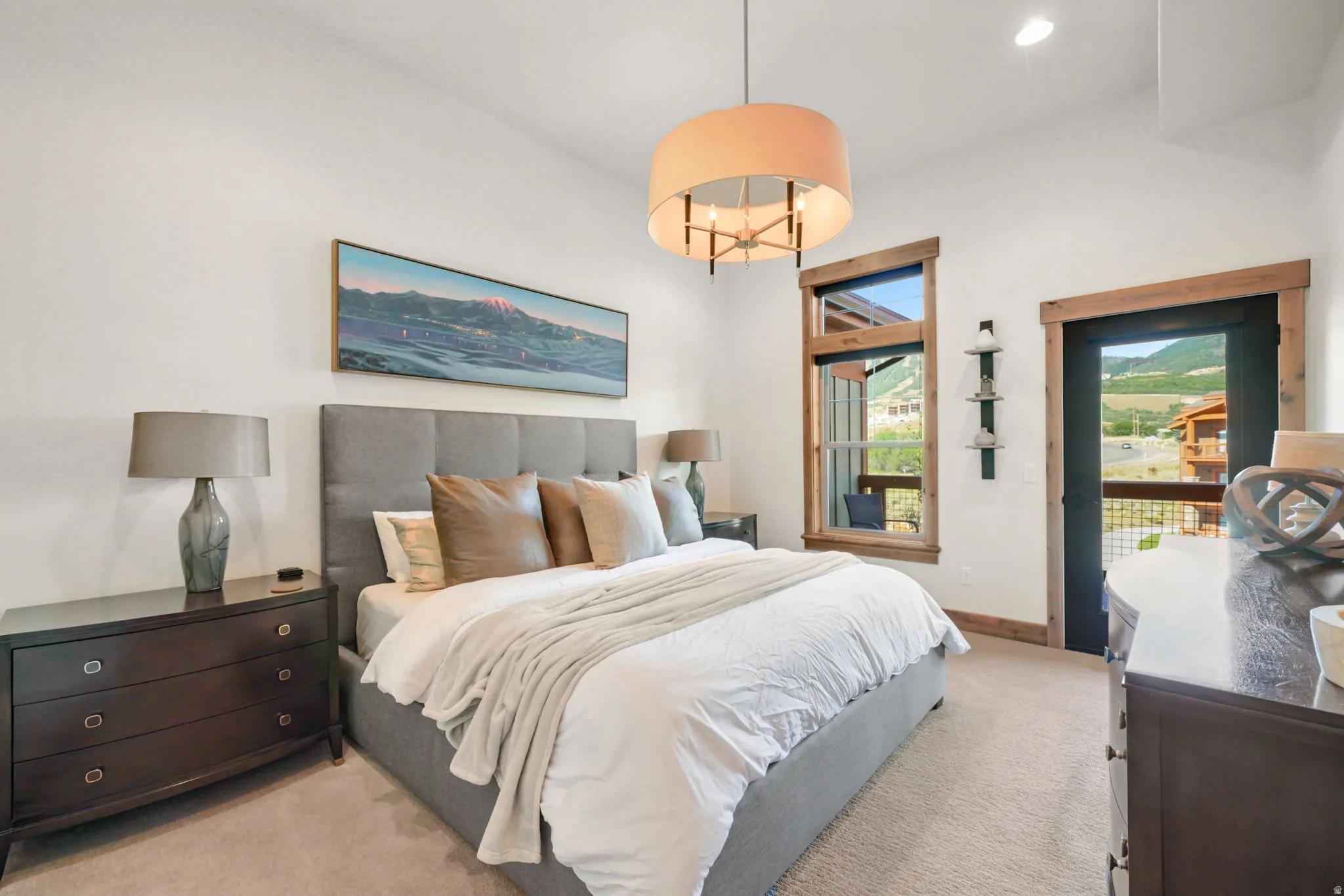Bedroom featuring a neutral color palette, plush carpeting, a fabric upholstered headboard, a contemporary chandelier, and a balcony door with rustic wood trim