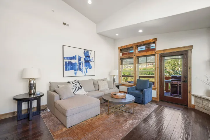 Living area featuring high vaulted ceilings, dark wood-finish flooring, recessed lighting, expansive windows with wood trim, and a glass-paneled door opening to an outdoor area
