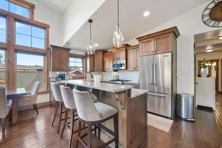 Kitchen featuring wood-finish flooring, wood cabinetry, stainless steel appliances, a center island with a light-toned countertop, and large windows with wood trim
